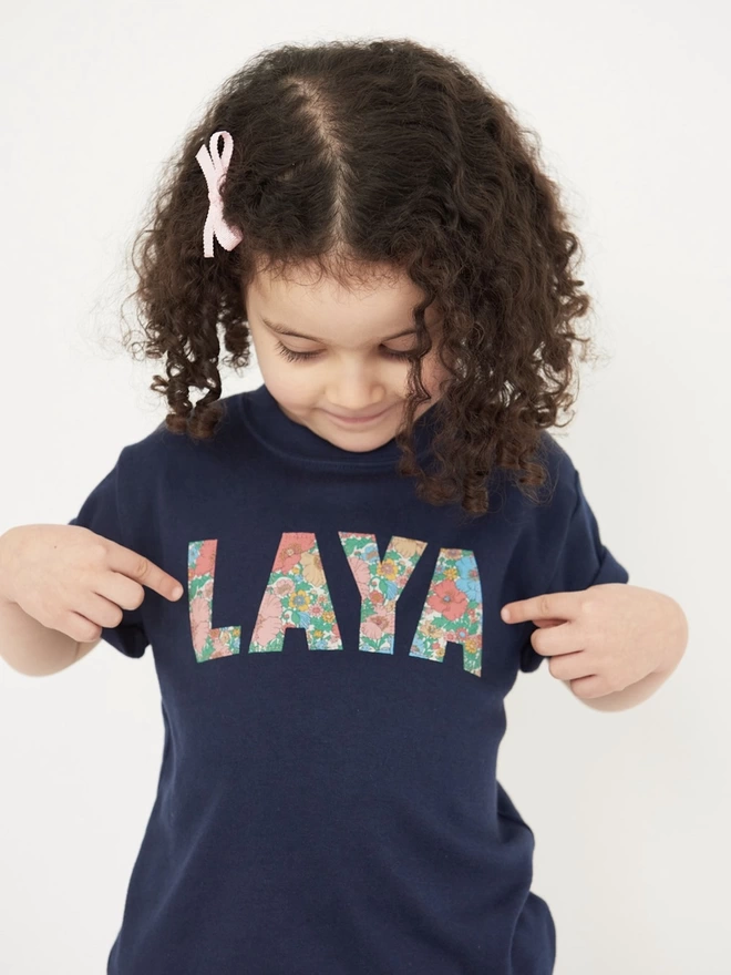 girl wearing a navy t-shirt with her name appliquéd on the front in Floral Liberty Print