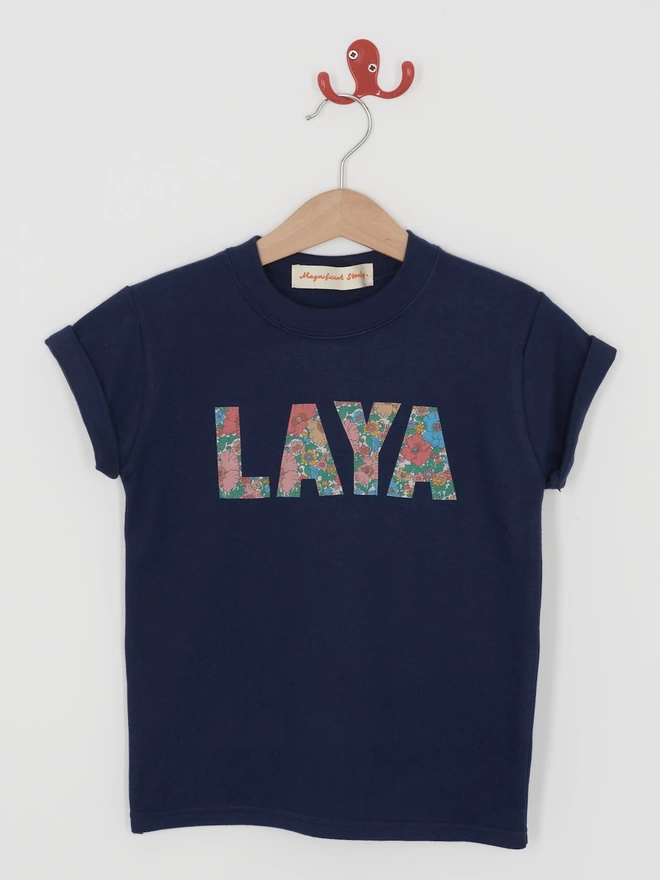  a navy t-shirt with the name Laya appliquéd on the front in Floral Liberty Print