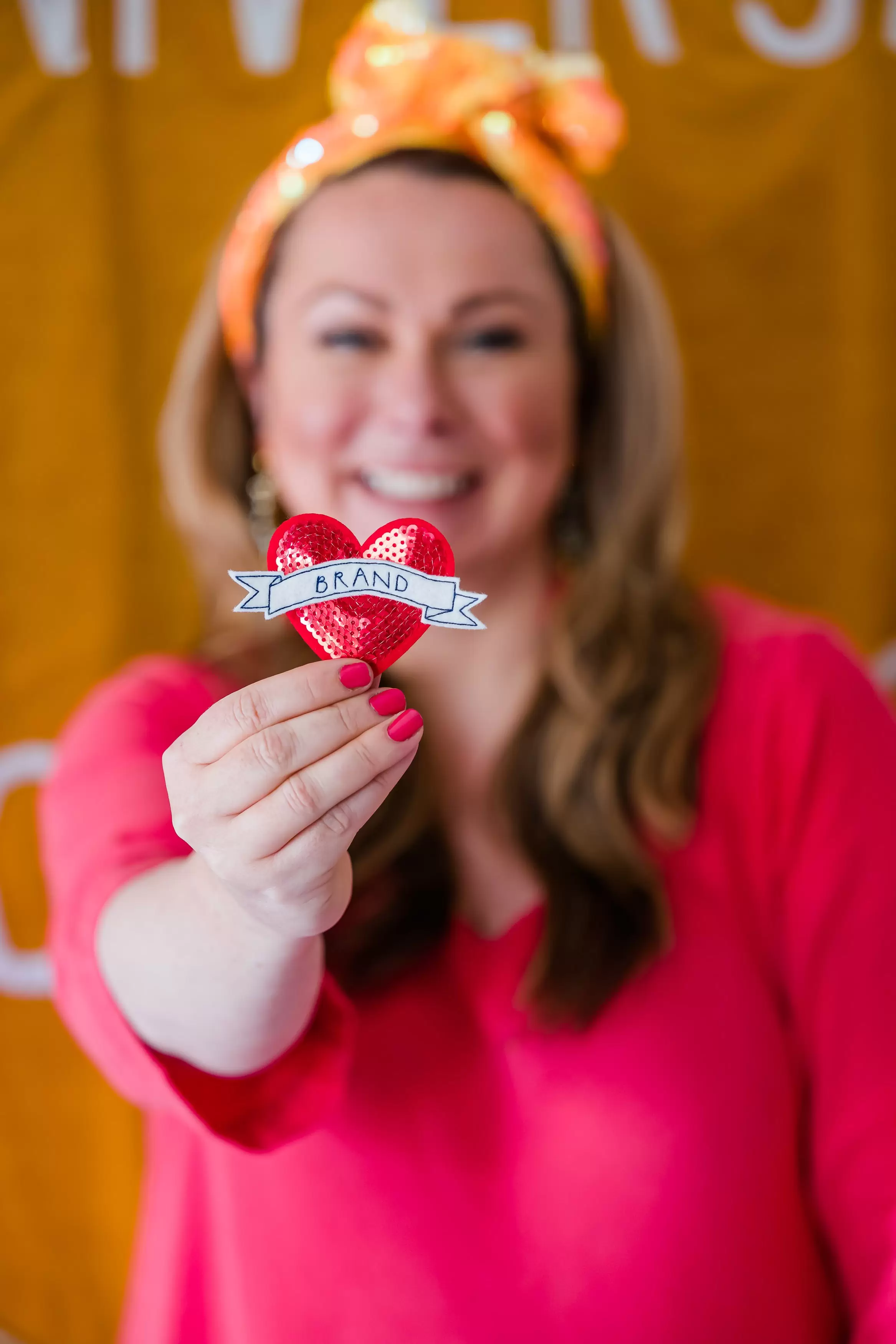 Holly Tucker, founder of Holly & Co, wearing a pink jumper and holding a Brand sequin heart. 