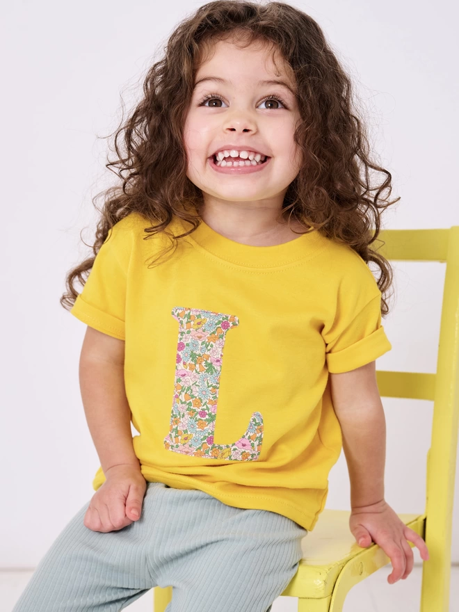a little girl in yellow t-shirt with floral initial on front