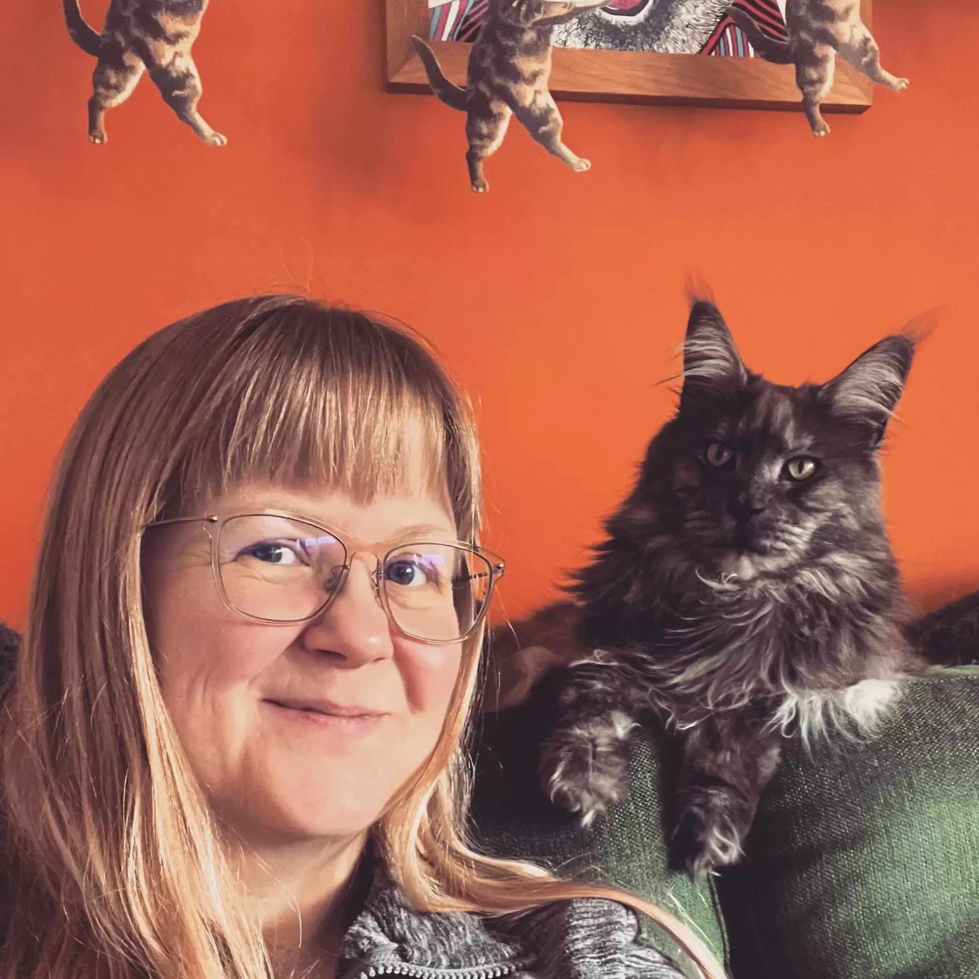 Claire Senior, owner and chief creator at The Curious Pancake sitting on her green, hipster sofa, looking directly at the camera. A little grey kitten sits to her right, gazing off dreamily into the middle distance. 