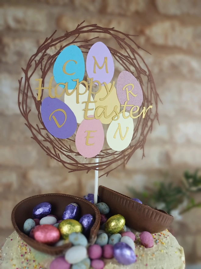 Easter cake topper featuring a brown nest filled with 8 different coloured easter eggs. All cut from paper.