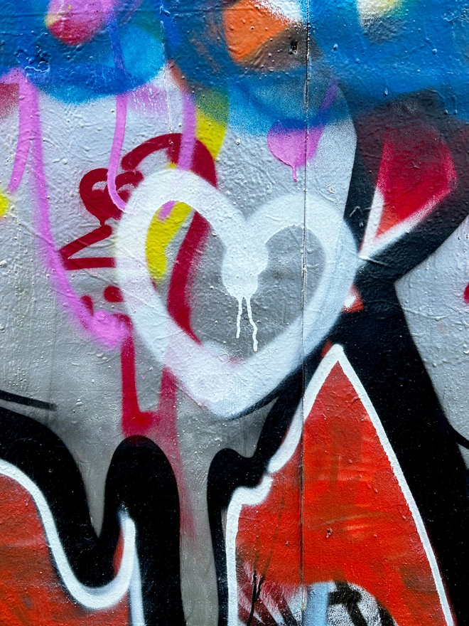 Photograph of a white spray paint heart with graffiti background taken by Evi Antonio, artist