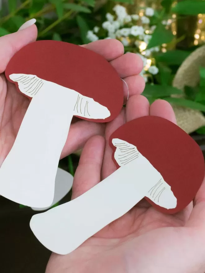 2 Mushroom Paper decorations held in models hand. Each decoration is slightly smaller than the palm of the model's hand