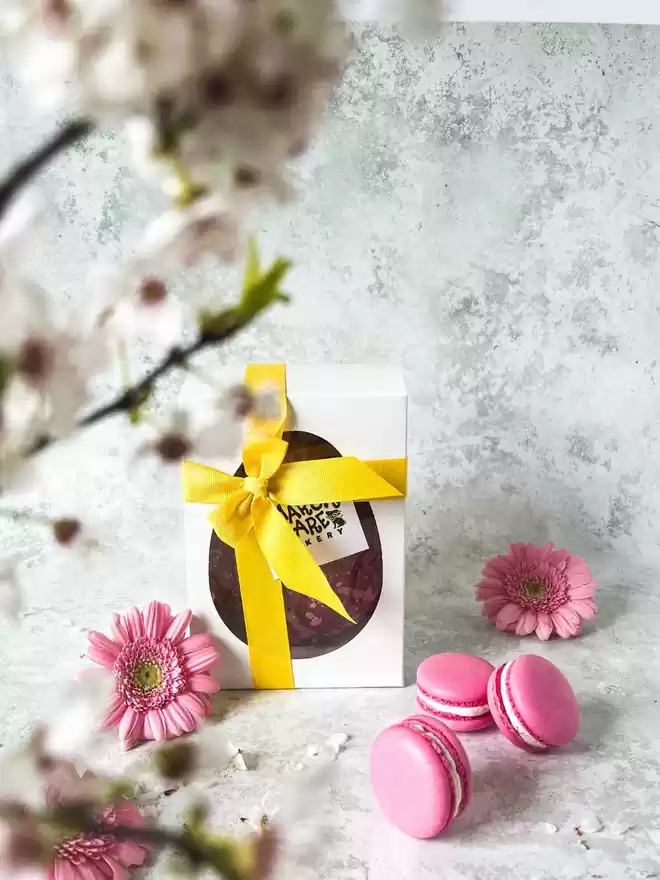 A pink easter egg with pink toasted marshmallow macarons in a gift box with flowers