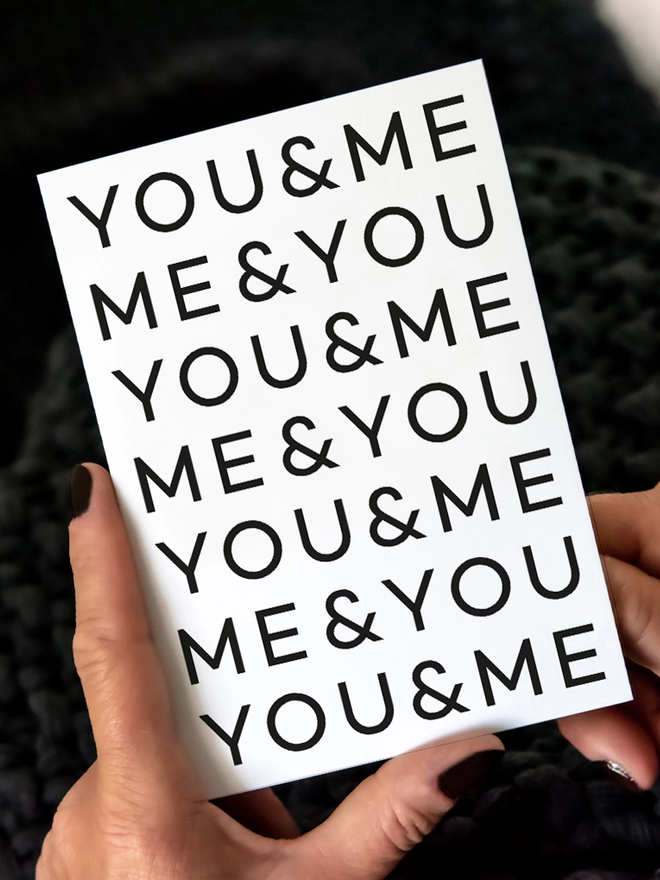 Lady starting to open a You & Me Anniversary Card on a dark background.