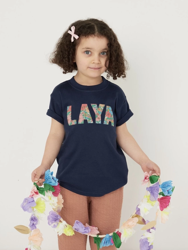 girl wearing a navy t-shirt with her name appliquéd on the front in Floral Liberty Print