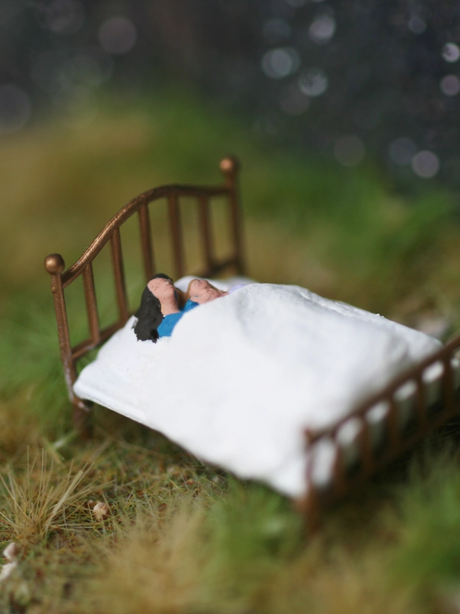 A diorama showing mother and daughter snuggling in bed in a forest