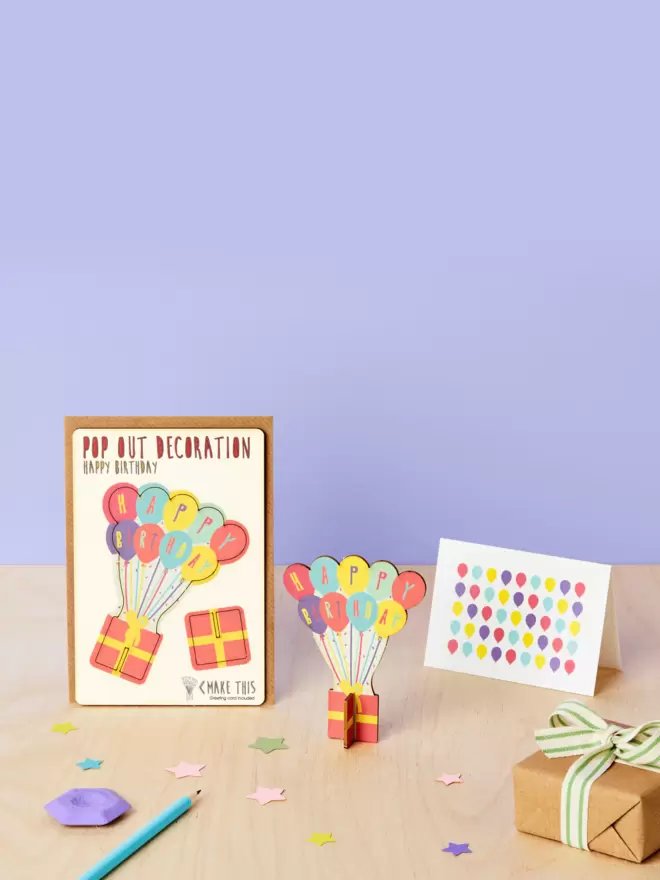 Birthday balloons birthday decoration and birthday balloon pattern birthday card and brown kraft envelope on top of wooden desk with lilac background