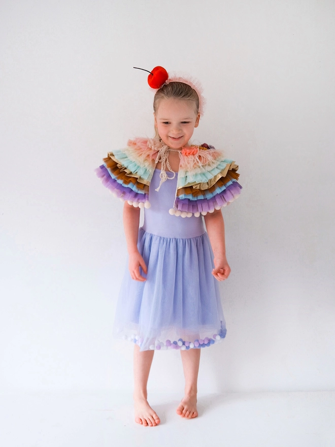 Young girl wearing a pom pom filled tutu dress and frilly cape.