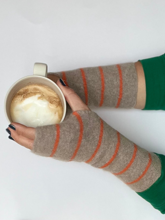 Knitted wristwarmers shown being on hands while holding a coffee cup