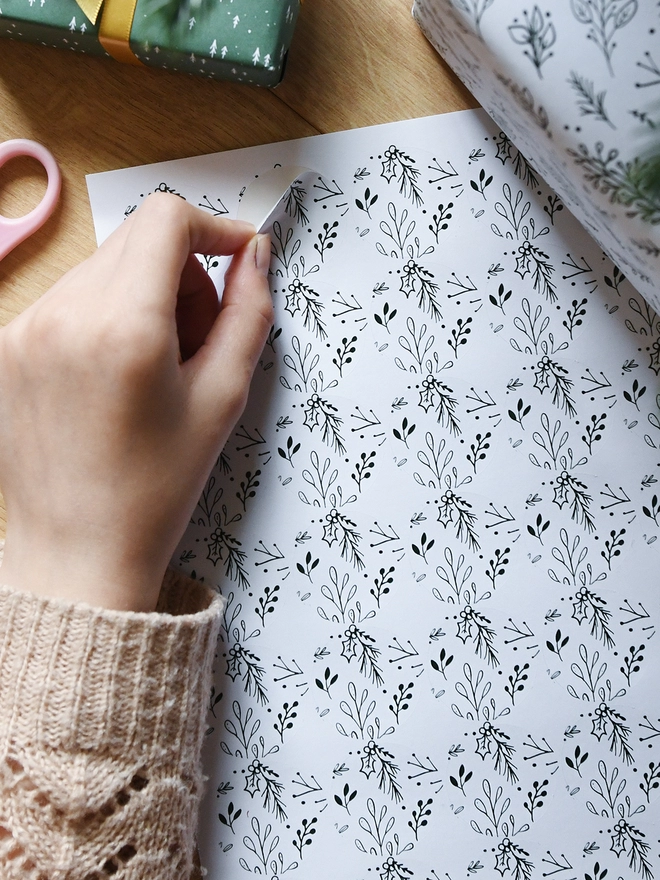 A hand peels a white sticker with a Christmas botanical design from a sheet of 35 matching stickers.