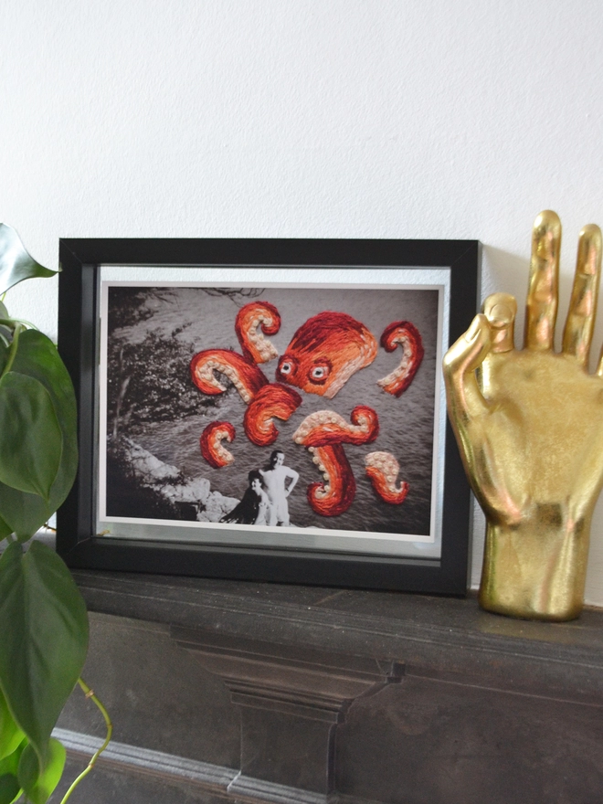 B & W photo of couple with embroidered octopus behind them, framed on mantlepiece