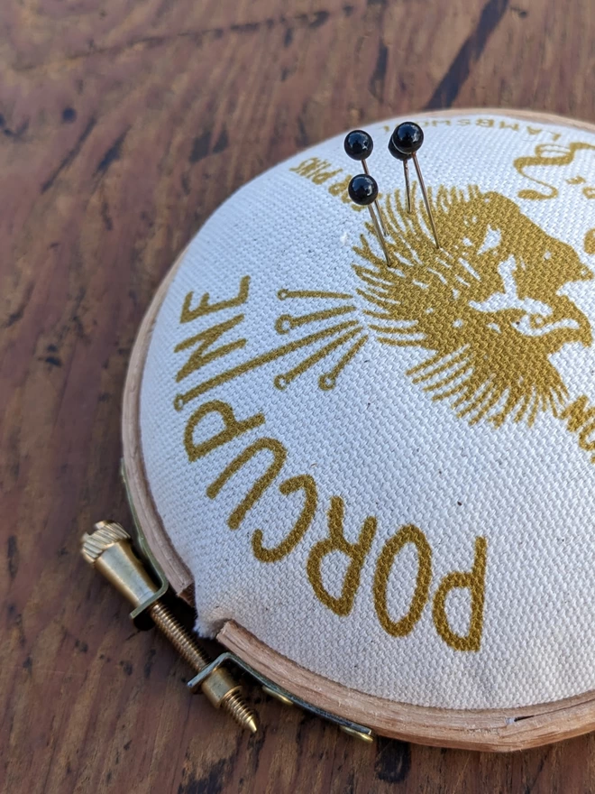 close up of mustard porcupine embroidery hoop pin cushion shown with pins.