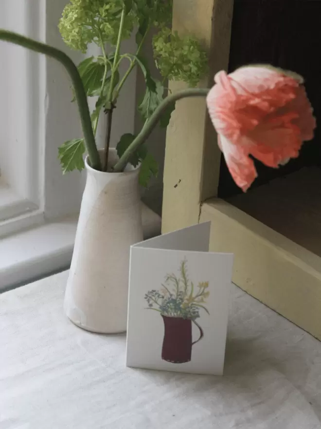 mixed bunch of flowers in a vase on a card next to fresh flowers. 