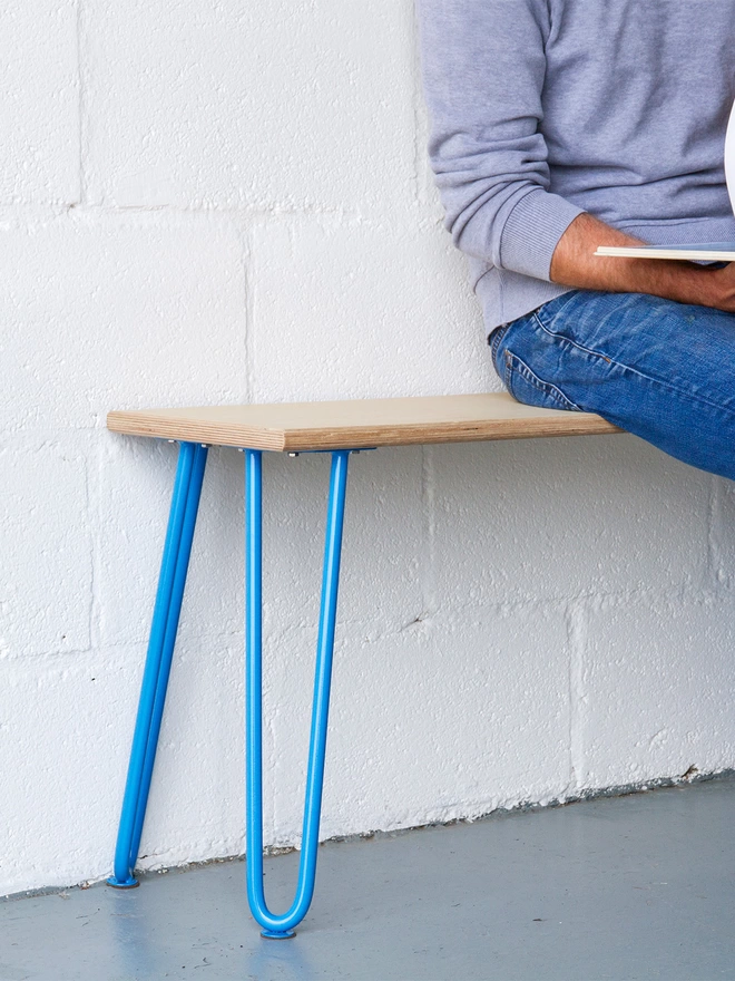 man in blue jeans sat on a hairpin leg bench with oak seat and light blue hairpin legs