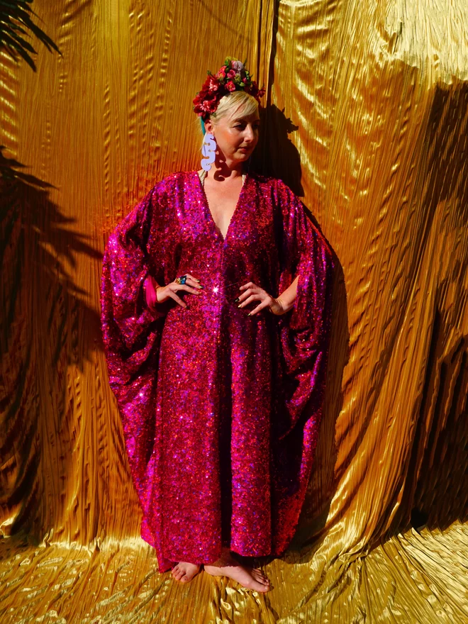 Cerise Holographic Sequin Kaftan seen on a woman with her hands on her hips looking to the side.