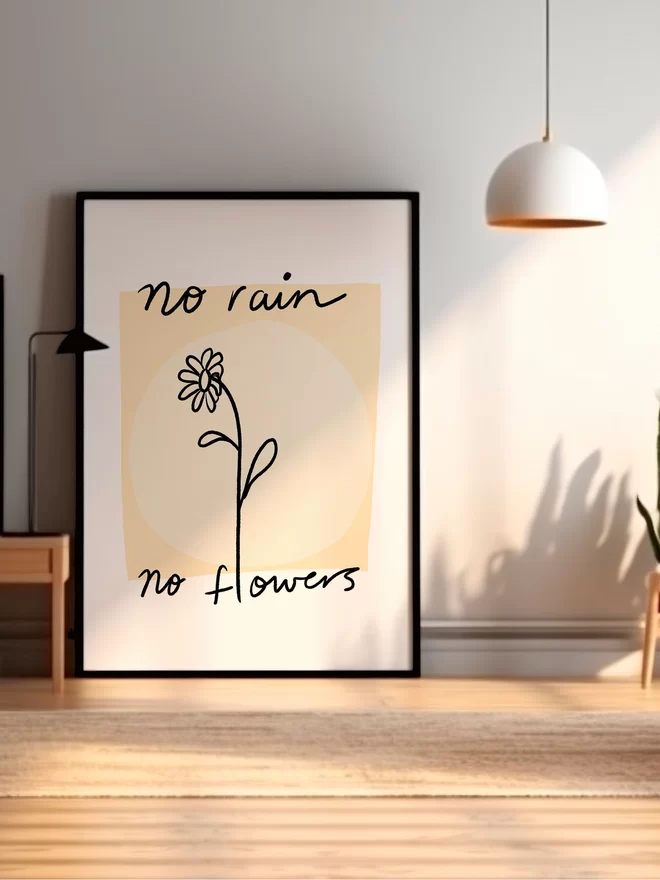 Frame sits against wall showing oversized print 'no rain no flowers' in black text with beige background