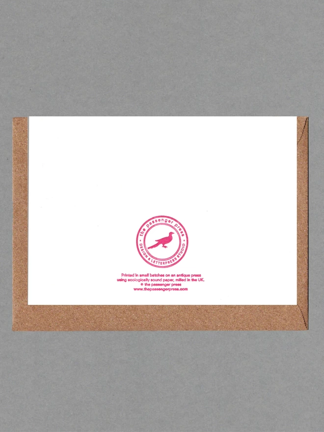 Back of white card with pink text on it with a brown envelope behind