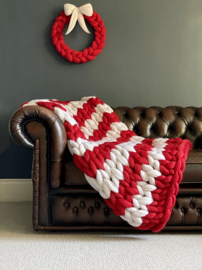 Bright red and white striped giant knitted merino blanket draped over the arm of a leather sofa