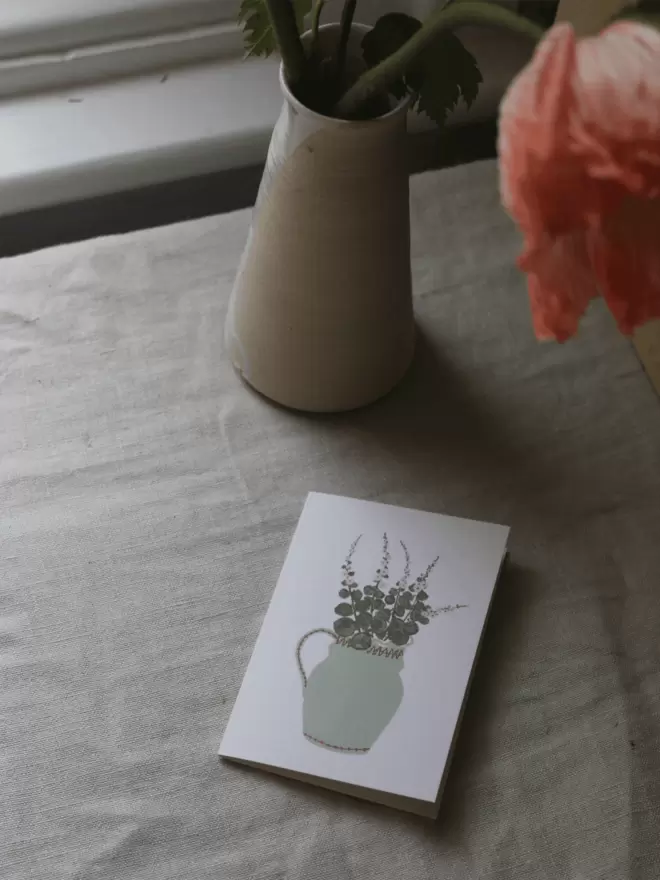 mini greetings card with cut hollyhocks on it arranged in a light green vase, next to a vase of icelandic poppise