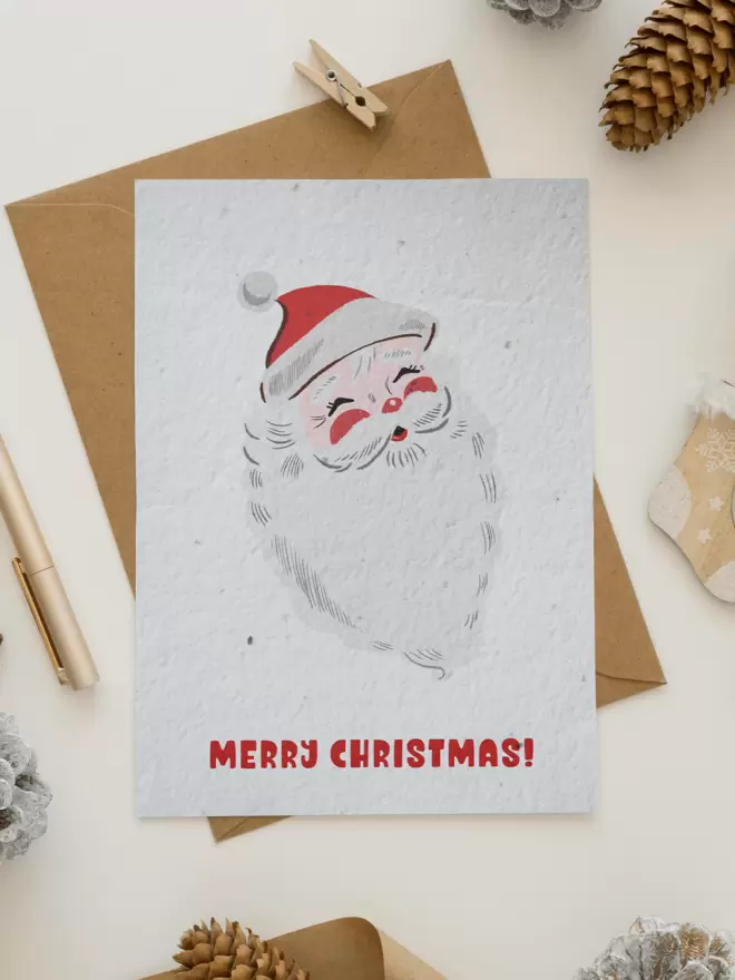 Christmas Card with an illustrated vintage style Santa surrounded by pine cones, a pen and a small peg