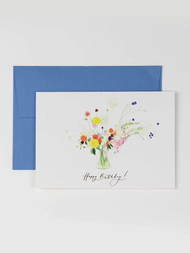 An illustrated greetings card with a corresponding blue envelope. The card features a finely painted colourful vase of flowers in yellow, pink and blue.