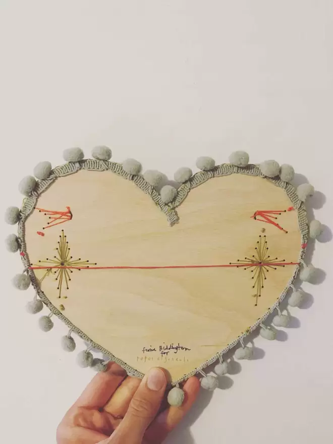 A hand shows the visible stitching on the back of the valentines heart, and thread to hang it from