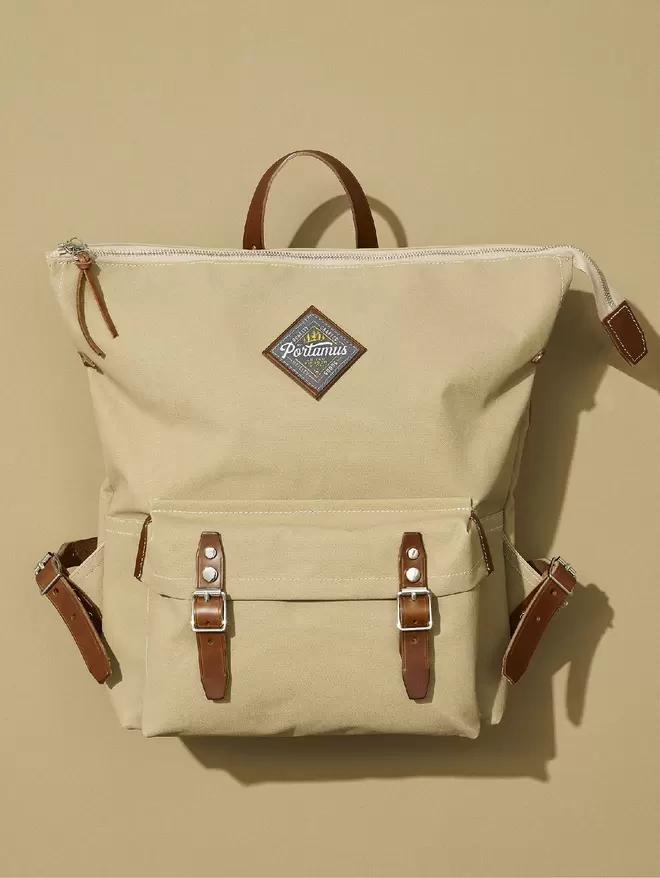 Taupe zip top backpack with brown leather trim and sliver hardware on taupe background.