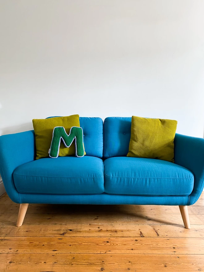 Cushion shaped like the letter M in Grass Green and Lilac