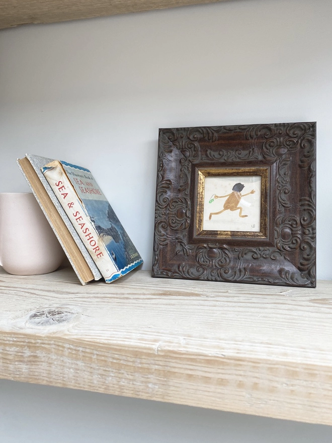 pale wooden shelf with framed drawing of naked man joyfully running on the beach 