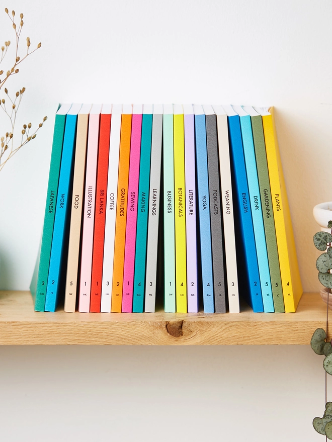 a bookshelf with lots of colourful notebooks with personalised text down the spine