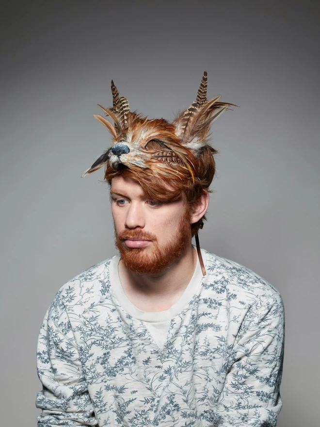Man wearing a luxury red fox masquerade mask atop his head as a headdress