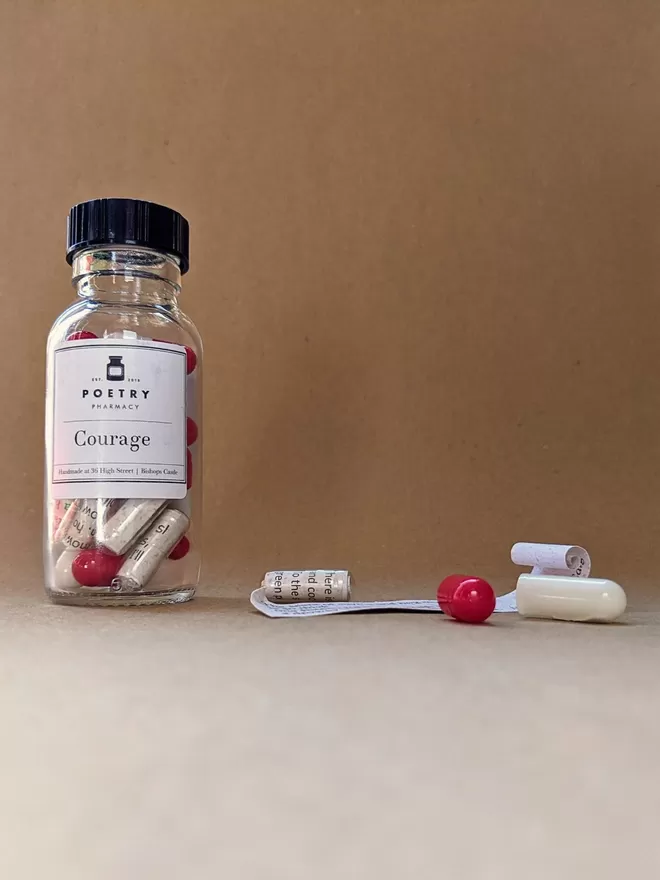 A glass bottle of red and white Courage poetry pills against a brown paper background