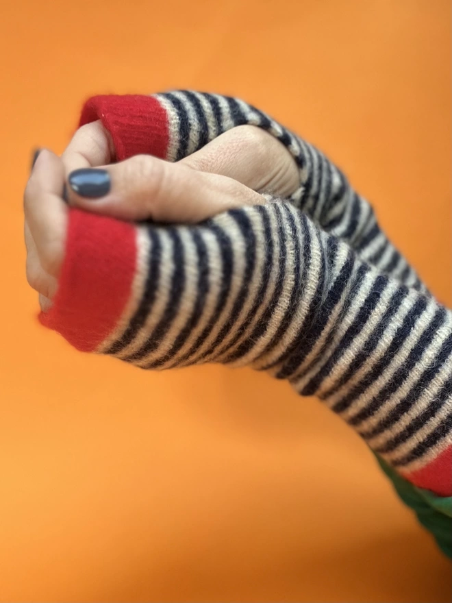 Knitted red navy striped wristwarmers worn with hands intertwined on an orange background