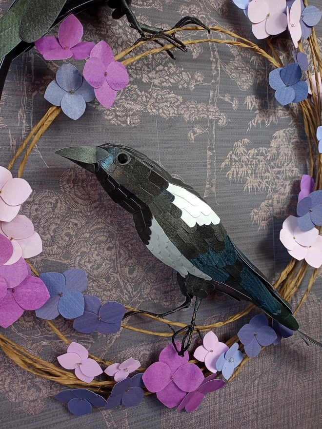 handmade sculpture of a magpie perched on a wreath of purple hydrangea flowers