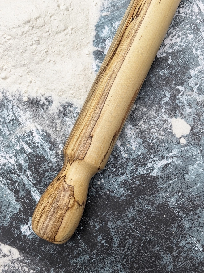 Close up of a stunning hand made rolling pin in Spalted Beech by Something From The Turnery, the picture is focussed on the darker brown all natural detailing along one end of the rolling pin.