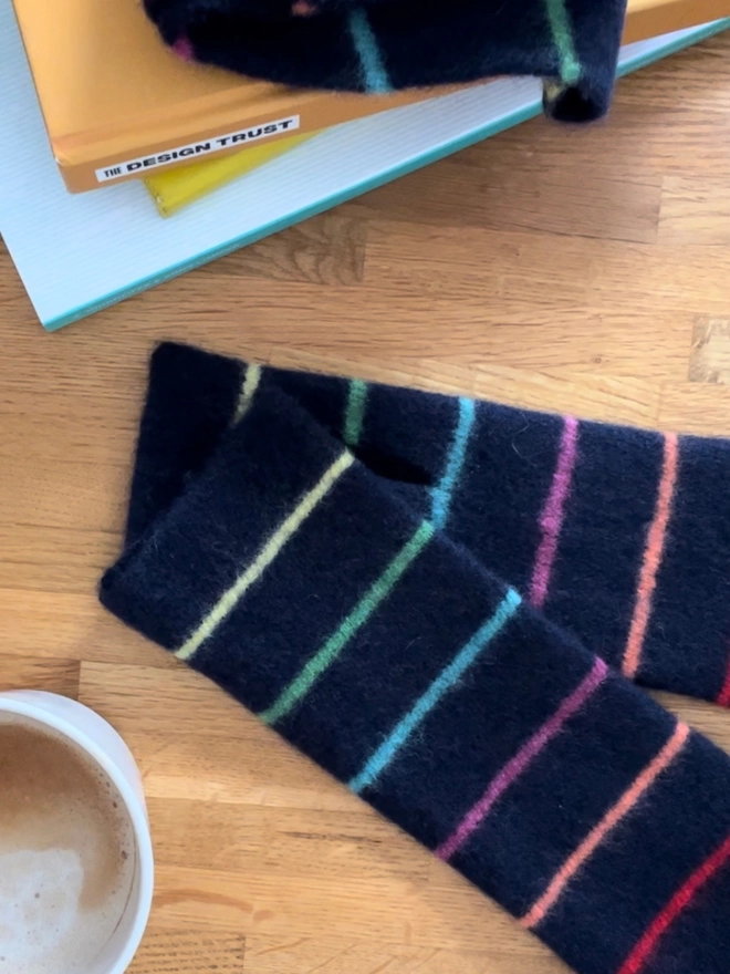 Knitted navy wristwarmers with multi coloured stripes laid flat on table