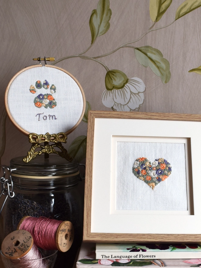 An embroidered Sunshine Garden Heart, displayed in an oak frame.  To the left is the embroidered cats paw.