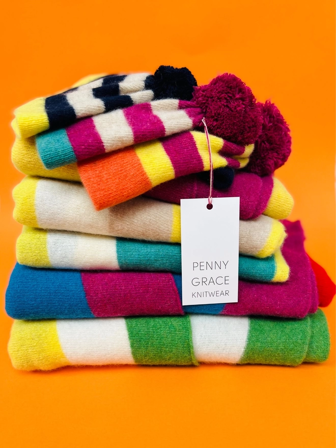 A stack of penny grace knitted accessories on an orange background