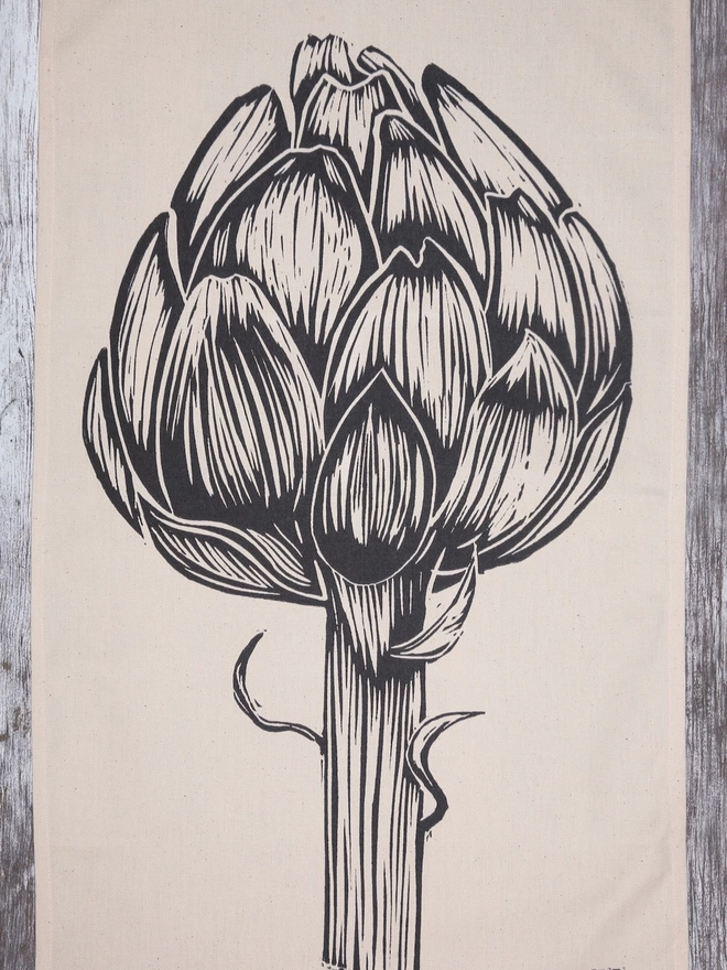 Picture of a tea towel with an image of an artichoke, taken from an original lino print