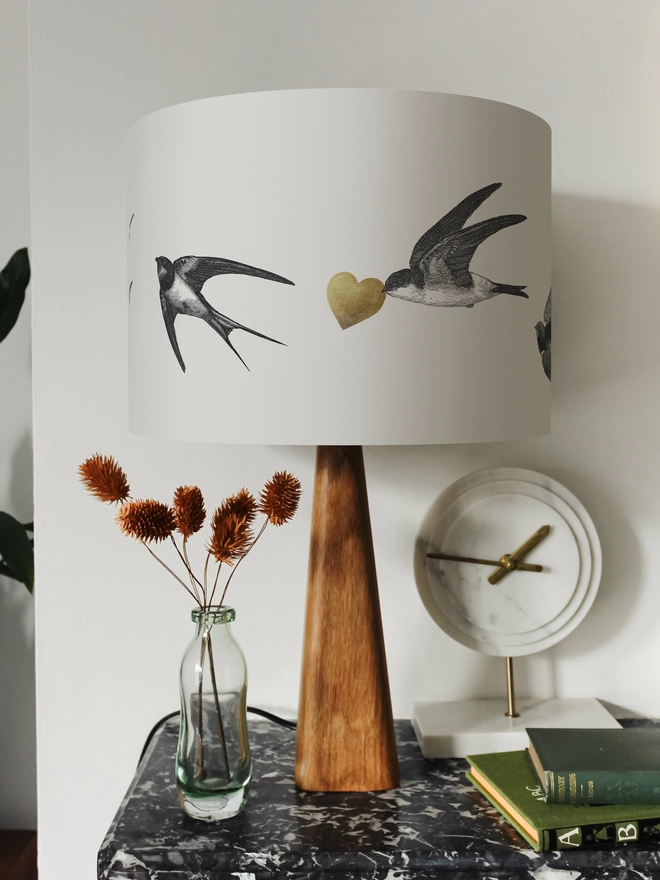 Drum Lampshade featuring Swallows on a wooden base on a shelf with books and ornaments