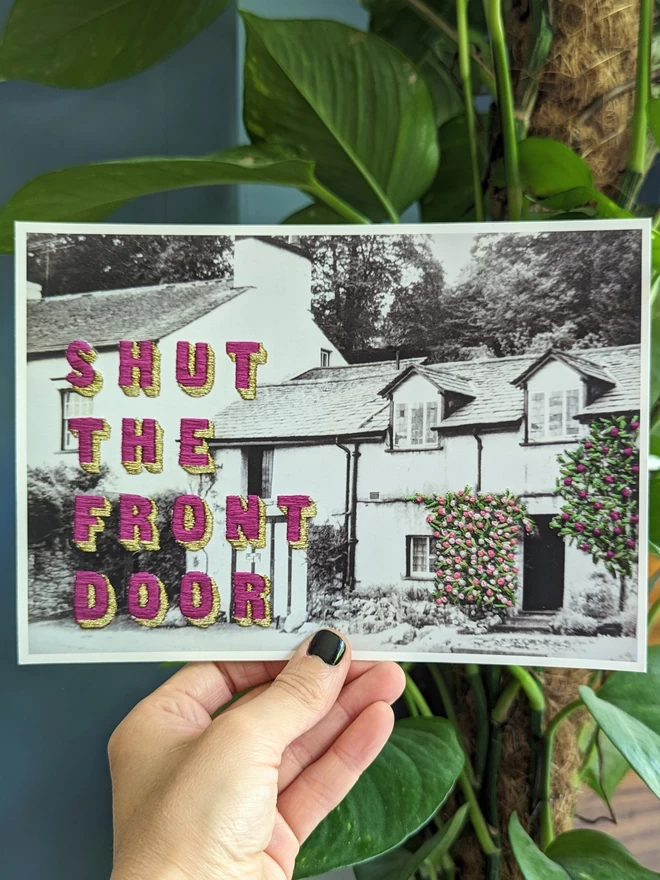 Print of Shut the front door embroidered on B&W cottage photo held 