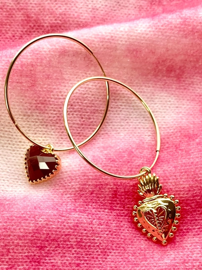 Pair of mismatching charm earrings with a Frida Kahlo Mexican heart and a read heart on a pink cashmere background