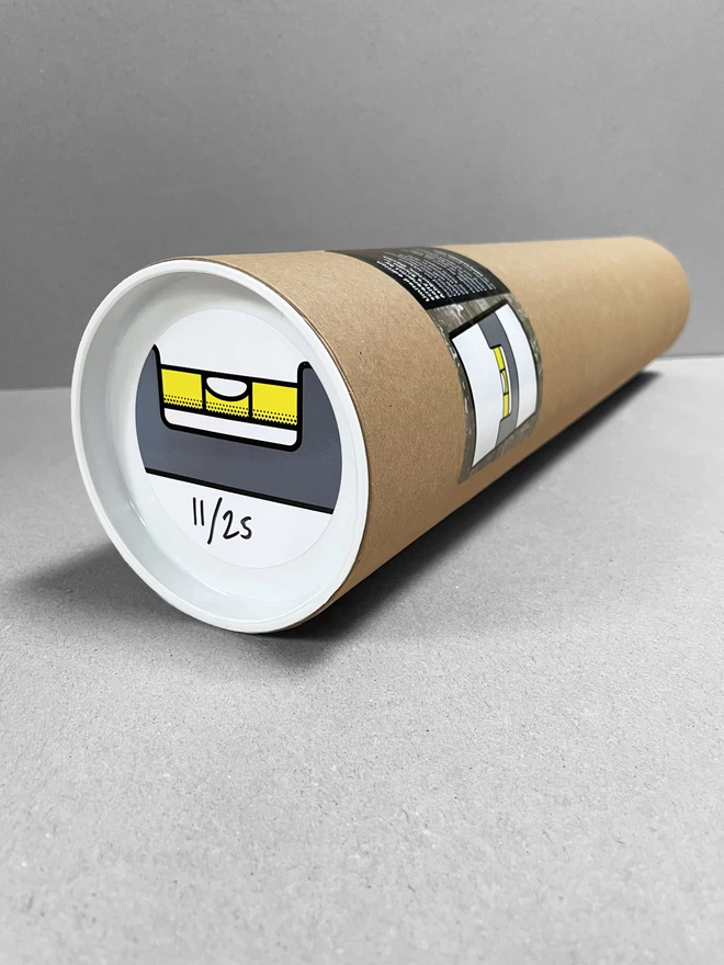 A cardboard tube laid on a plain grey background, containing the spirit level print with a sticker on the end depicting that.