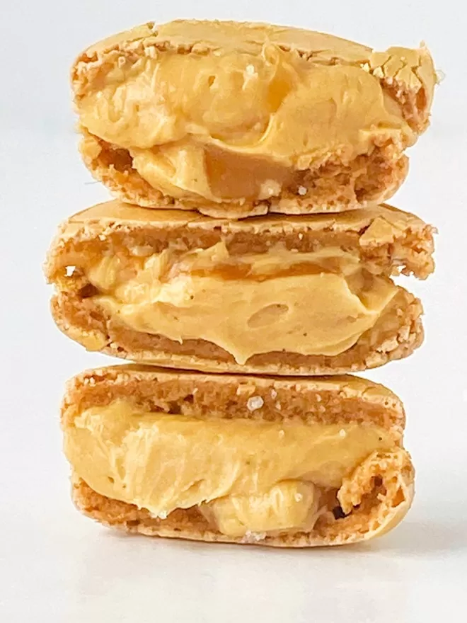a stack of three golden macarons sitting on top of each other, cut in half to show the inside gooey caramel filling