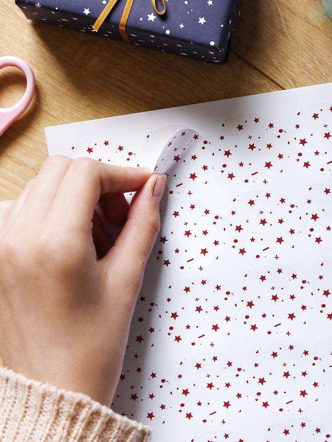 A hand is peeling a white sticker with a red star design from a sheet of 35 matching stickers.