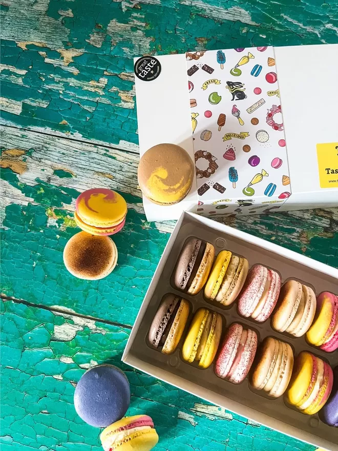 a box of colourful macarons sitting on top of a green wooden table