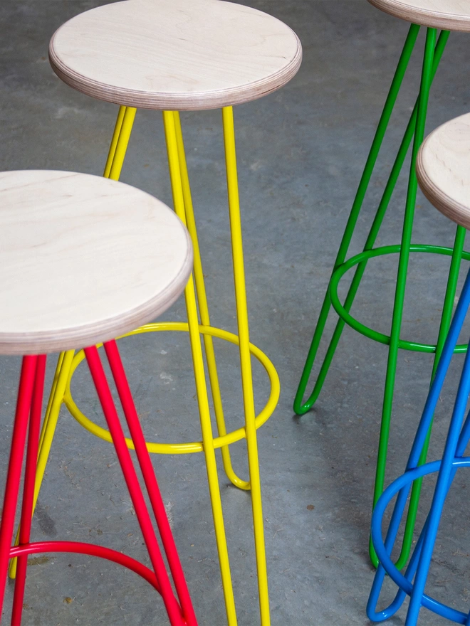 set of four hairpin leg bar stools with plywood seats and different brightly coloured legs - one red, one yellow, one green and one blue
