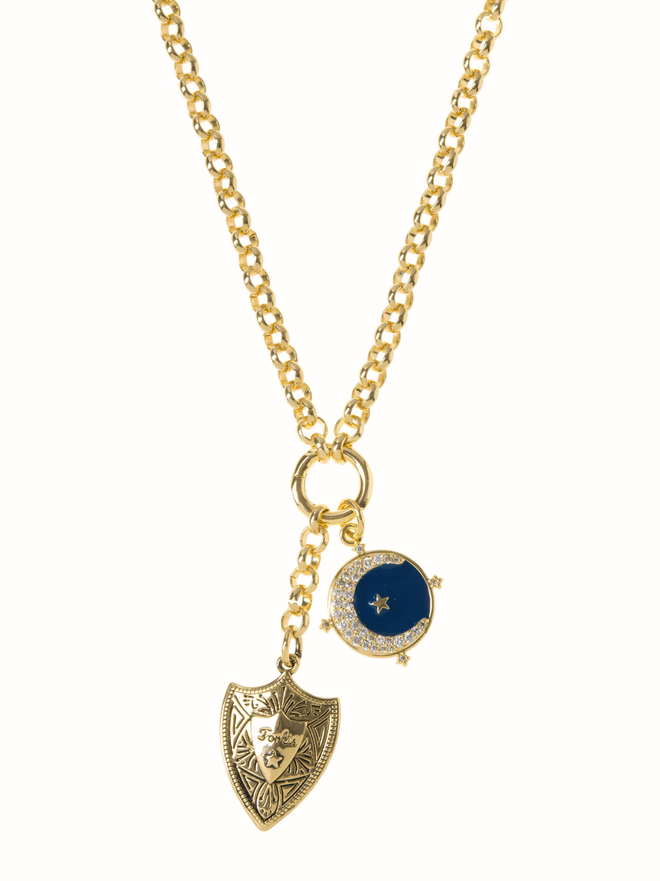 Gold shield and pave set crescent moon charm hanging from gold belcher chain against a white background